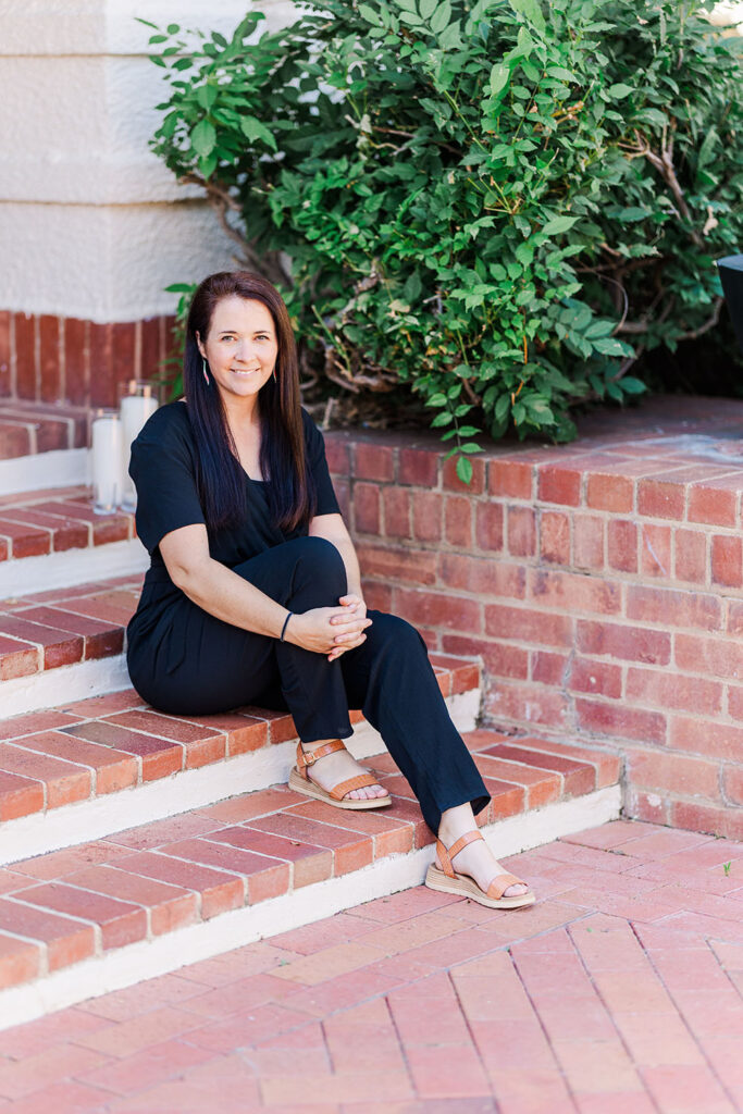 white woman with brown hair in black suit on red brick stairs
